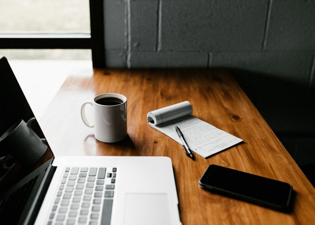 A laptop, notebook and coffee on a desk while comparing platforms